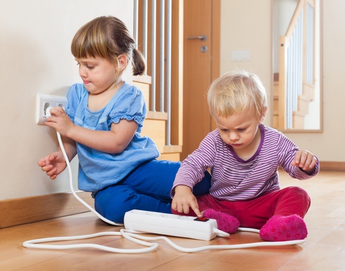Two children  playing with electrical extension and outlet on floor at home