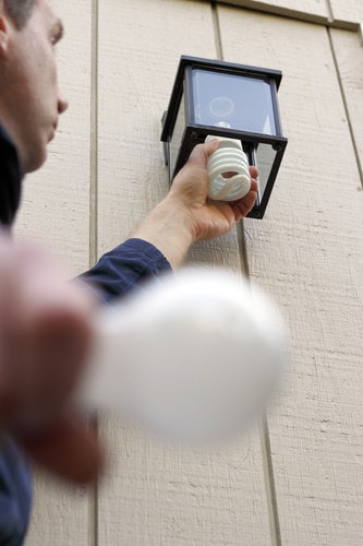 Male carefully replacing an old incandescent lightbulb with a new compact fluorescent light in an outdoor fixture to save money when the lamp is on.
