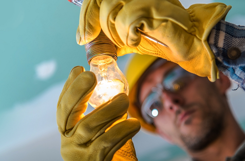 Electrician wearing a yellow hat and gloves while holding a light bulb