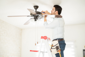 Technician standing on ladder while repairing ceiling fan