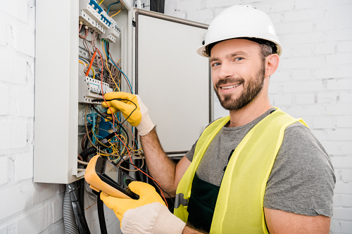 Technician wearing gloves and safety gear while inspecting an electrical panel