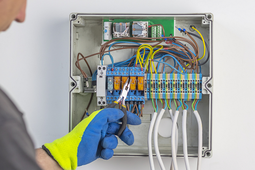 Technician wearing blue and yellow gloves and inspecting electrical panel wiring